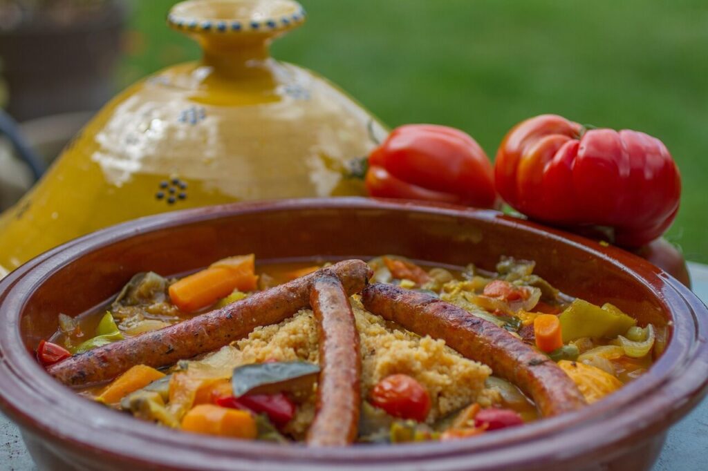 Cous cous con merguez, verdure e spezie servito in una tajine di terracotta, tipico piatto della cucina nordafricana.