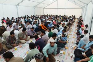 Un gruppo di uomini riuniti sotto una tenda per condividere l'iftar durante il Ramadan, con cibo e bevande disposti su lunghi tappeti.