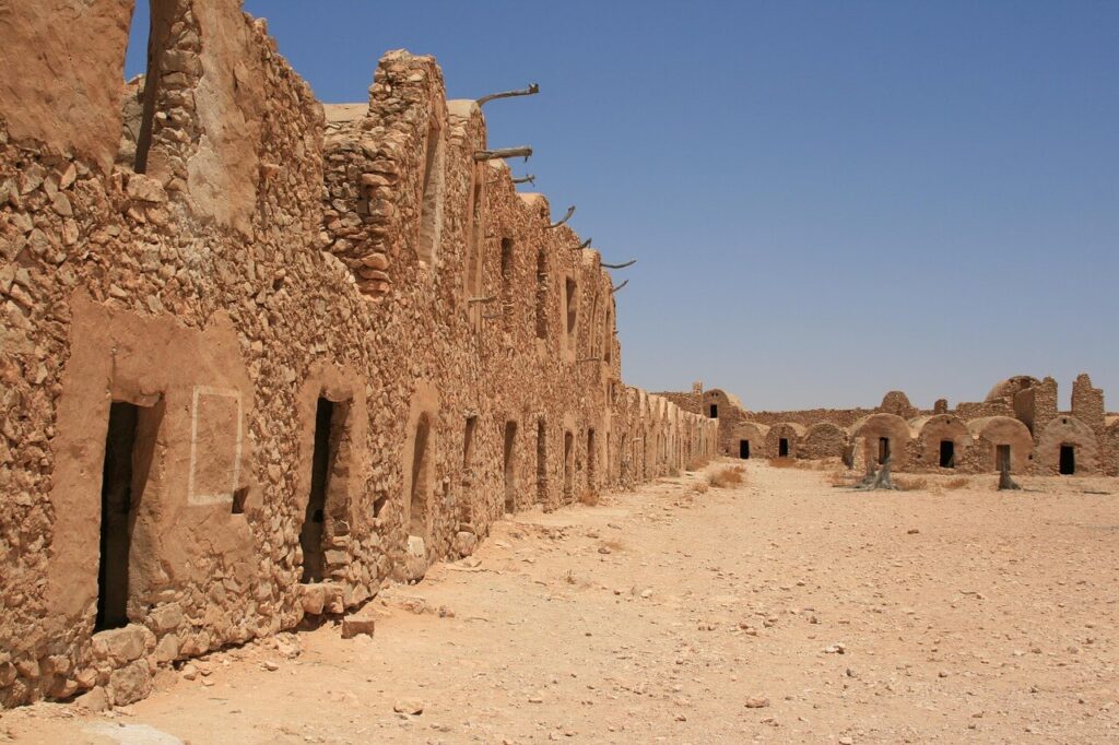 Rovine di un antico ksar berbero in Tunisia, con edifici in pietra e porte scavate nella roccia sotto un cielo limpido nel deserto.