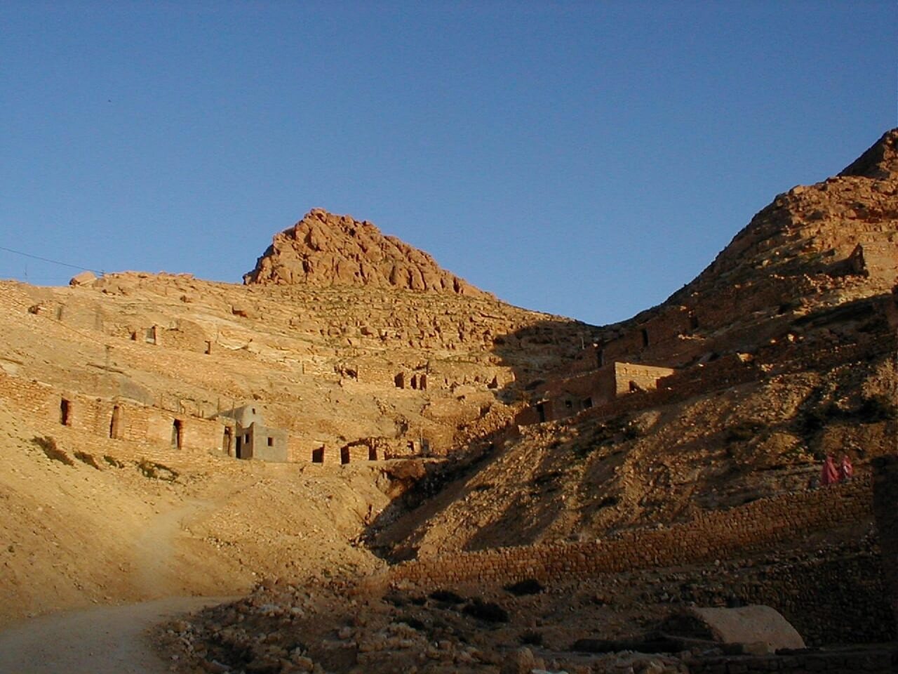 Berber village in Tunisia built on the slopes of a mountain, with stone houses integrated into the desert landscape under a clear sky.