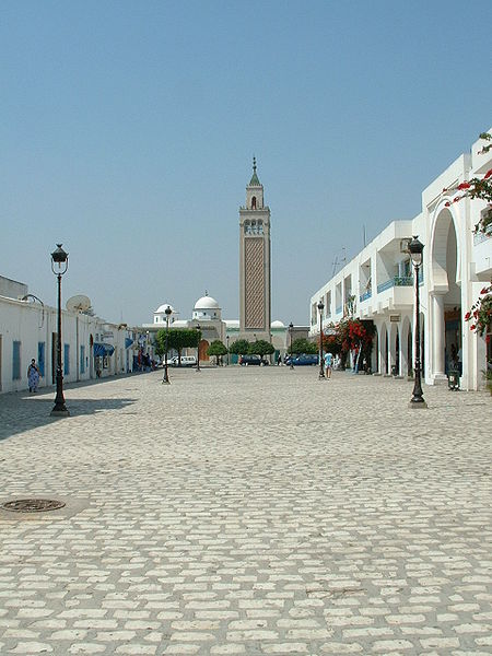 La Corniche di La Marsa in Tunisia con vista sul mare, una lunga passeggiata con balaustra bianca e persone sedute sotto un cielo parzialmente nuvoloso.